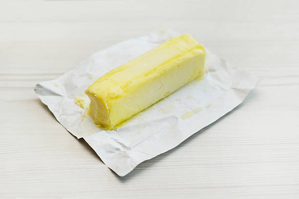 Closup of a stick of butter on a whitewashed wood table.