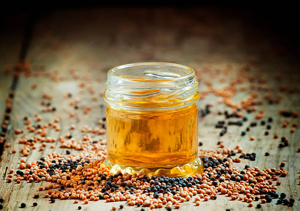 Oil of mustard in a small jar and yellow and black mustard seeds on an old wooden table in rustic style, selective focus